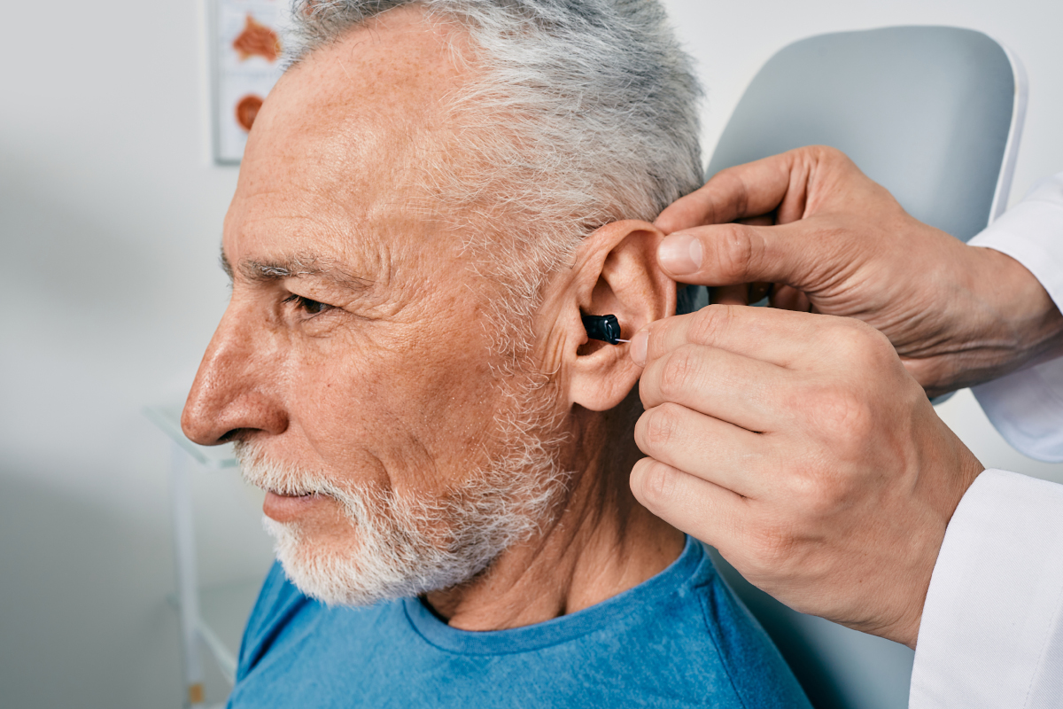 Grey-haired elderly man during installation intra-ear hearing aid into his ear by his doctor audiologist, close-up. Hearing treatment for hearing impaired people
